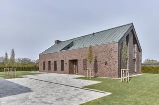 Perspektivische Außenaufnahme eines modernen Architektenhauses mit roter Backsteinfassade und Metall­dach.